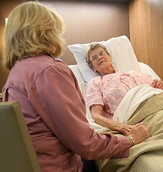 Woman sitting beside an elderly lady in a bed