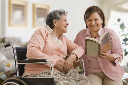 Older woman reading to an elderly lady in a wheelchair