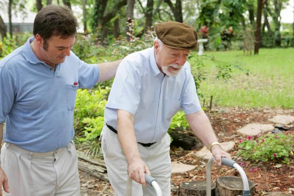 Senior man caring for an elderly man with a walker in a garden